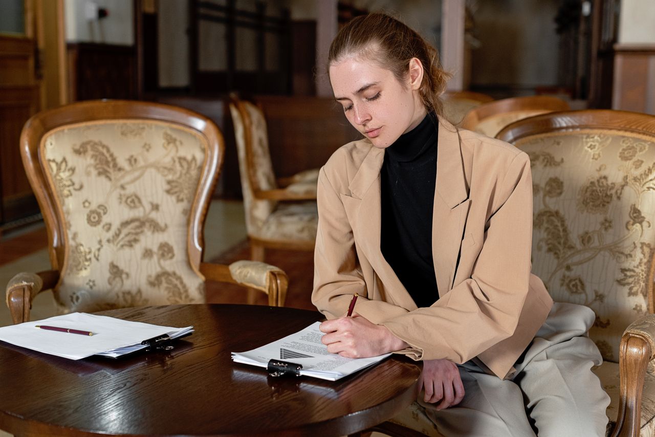 why-choose-us Young woman in a brown blazer signing documents at a table in a stylish office.