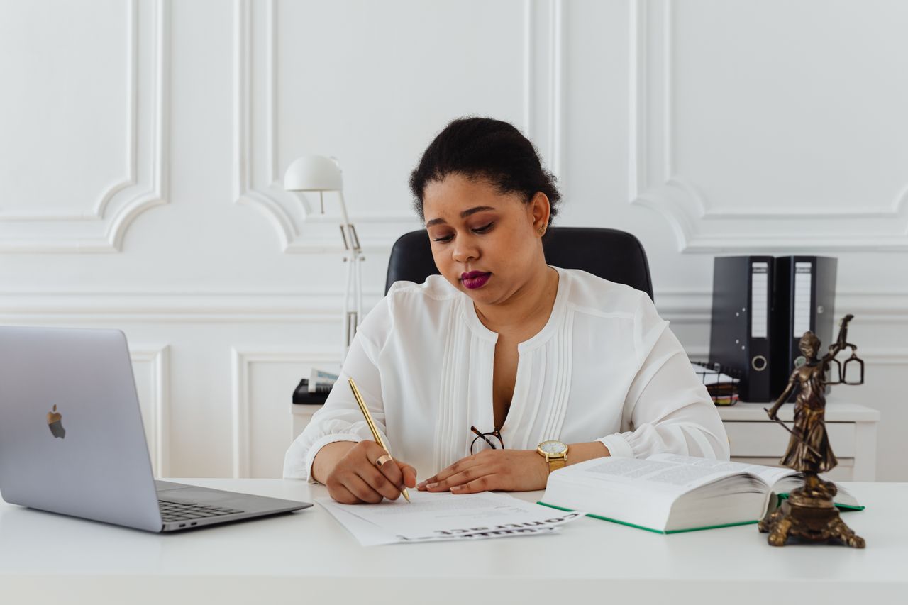 services-03 African American woman lawyer signing documents at a desk, symbolizing professionalism.